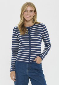 Cardigan a rayas en azul marino y crema con cierre de botón, puños acanalados y cuello redondo. Tejido suave y diseño ajustado.