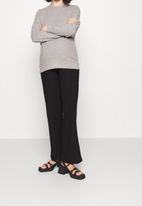 Sudadera gris de manga larga con dobladillo acanalado, pantalones de pierna ancha negros y sandalias de plataforma negras con múltiples correas y tacones gruesos.