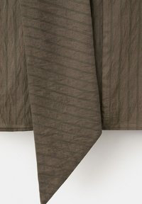 Tissu marron avec de fines rayures horizontales et verticales foncées, suspendu avec une extrémité triangulaire pointue sur un fond blanc.