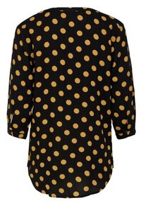 Blouse noire à manches longues et coupe ample, ornée de grands pois jaune moutarde et d'un ourlet arrondi.