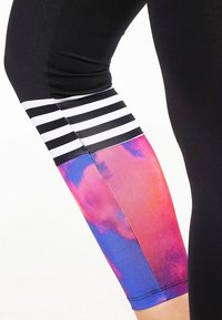 Černé legíny s proužkovaným černobílým pásem na spodní části nohy, zdobené barevným abstraktním vzorem v růžové a modré barvě.