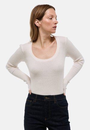 Body à manches longues côtelé en crème clair, avec un décolleté large et une silhouette ajustée, associé à un jean taille haute foncé.