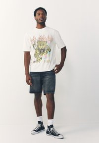 White graphic t-shirt featuring a leopard design, paired with dark denim shorts and black high-top sneakers with white socks.