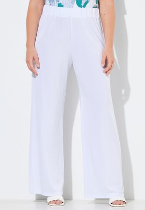 Vrouw draagt hoge taille, wijd uitlopende witte broek met elastische tailleband en zijzakken, gecombineerd met witte open teen hakken.