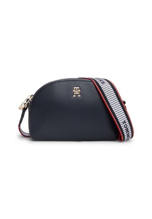Sac bandoulière demi-lune bleu marine avec logo doré et large sangle réglable blanche, noire et rouge avec texte de marque.