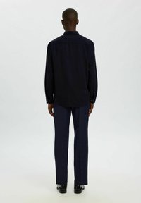 Ciemnoniebieska koszula z długim rękawem i kołnierzykiem zapinanym na guziki, prosto cięta, o dopasowanym kroju, zestawiona z dopasowanymi spodniami i butami.