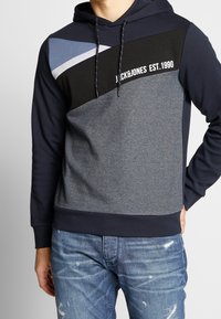 Blå och grå färgblockerad hoodie med dragsko i huvan, logotekst och ribbade muddar och nederkant, tillverkad av en mjuk tygblandning.