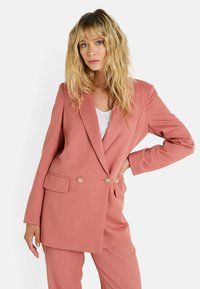 Blazer rose avec une coupe ajustée, fermeture à double bouton avec des accents floraux, et poches latérales, associé à un pantalon assorti.