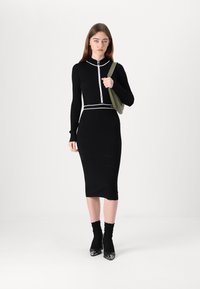 Melnas ribotas kleitas ar rāvējslēdzēju, baltas akcenti apkaklē un jostā, apvienotas ar melniem augstiem apaviem un teksturētām melnām zeķēm.