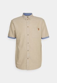 Camisa de manga corta en lino beige con cuello y puños azules, que cuenta con un bolsillo en la parte frontal y un detalle de etiqueta marrón. Botones en color a juego.