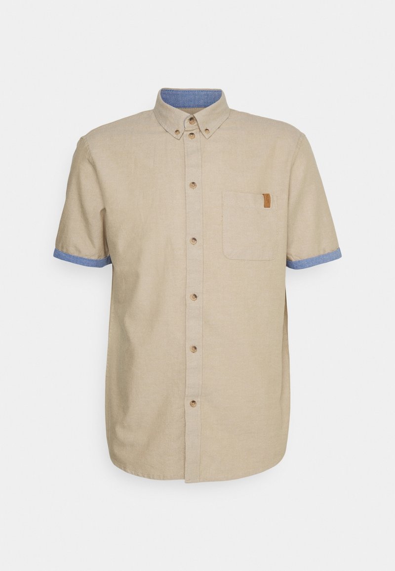 Camisa de manga corta en lino beige con cuello y puños azules, que cuenta con un bolsillo en la parte frontal y un detalle de etiqueta marrón. Botones en color a juego.