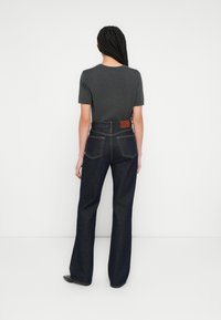 Top gri cu mâneci scurte, asortat cu pantaloni evazați din denim închis, cu talie înaltă. Pantalonii au buzunare în spate și o emblema din piele maro cu logo.