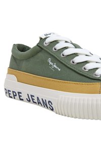 Zelené plátěné tenisky s bílými tkaničkami, béžovými akcenty a bílou podrážkou. Na boku mají označení "PEPE JEANS". Navrženo pro volnočasové nošení.