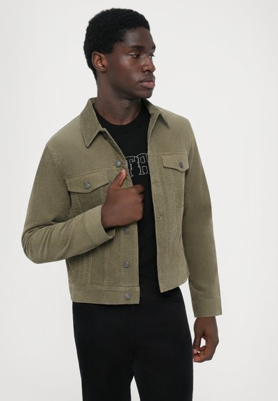 Jachetă din catifea de culoare verde măsliniu, cu front butonat, două buzunare pe piept și o croială ușor scurtă, asortată cu un tricou negru.