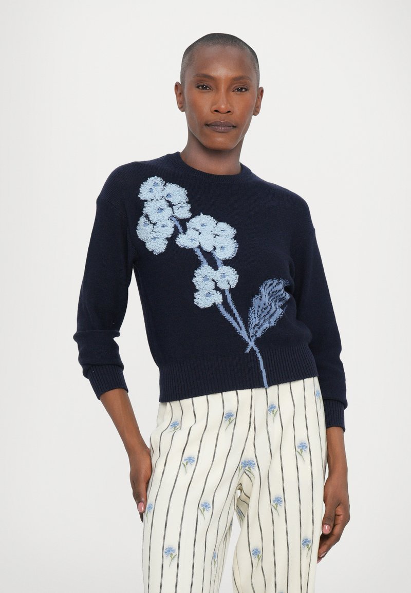 Navy knitted sweater featuring light blue floral embroidery on the front. Rounded neckline and long sleeves. Paired with striped floral pants.