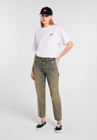 T-shirt bianca oversize con un piccolo logo; jeans blu sbiaditi con vestibilità dritta; cappellino nero; sneakers nere con accenti bianchi.