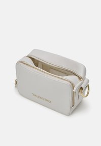 Vit läder crossbody-väska med guldfärgad hårdvara, rektangulär form, dragkedjestängning och präglad logotyp på framsidan. Strukturerad yta.