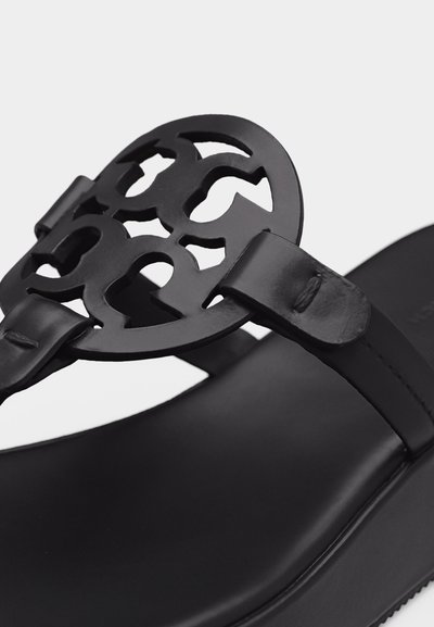 Μαύρο δερμάτινο σανδάλι με διακοσμητικό λογότυπο σε σχήμα κυκλικού ανοίγματος κοντά στο λουράκι των δαχτύλων, σε λείο πέλμα.
