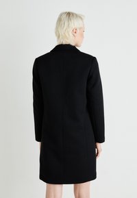 Čierny vlnený kabát s upraveným strihom, dlhými rukávmi a klopovým golierom, s hladkou textúrou a bez viditeľného hardvéru.