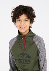 Groene half-zip pullover met grijze mouwen, voorzien van een berggrafiek en de tekst "PROTEST OUTERWEAR". Het heeft een rode rits en een zachte textuur.
