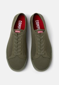 Ténis de malha verdes com uma superfície texturizada, apresentando um design de atacadores e um interior vermelho com o logótipo "Camper" na língua.