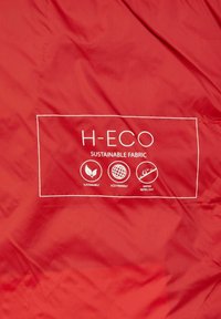 Roter Stoff mit dem "H-ECO"-Logo, gekennzeichnet als nachhaltiger Stoff, mit Symbolen, die anzeigen, dass er nachhaltig, umweltfreundlich und wasserabweisend ist.