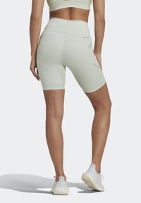 Shorts de ciclismo de talle alto en color verde menta, hechos de material elástico con textura suave y bolsillos laterales, combinados con zapatillas deportivas blancas.