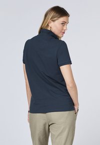 Dunkelblaues Poloshirt mit umgeschlagenem Kragen und kurzen Ärmeln, kombiniert mit hellbeigen Hosen. Glatte Baumwollstruktur, minimalistische Details.