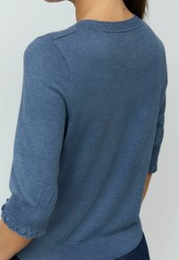 Suéter de punto azul con mangas de tres cuartos, que presenta un cuello acanalado y puños ondulados. Textura suave, corte ajustado y diseño liso.