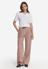 Vit kortärmad V-ringad topp som matchas med lösa, ljusrosa vida byxor. Outfiten har ett brunt bälte och mörka loafers.