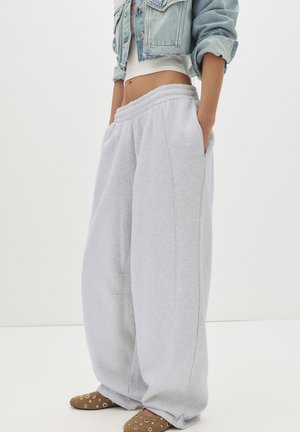 Person wearing baggy light gray sweatpants, white crop top, light blue cropped denim jacket, and brown slip-on shoes with metal eyelets.