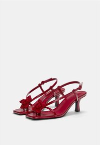 Escarpins à talons slingback en cuir rouge avec des bouts carrés, ornés d'accents floraux tricotés et de fines lanières, reposant sur un petit talon noir.