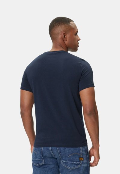 Laivansinis puuvillapaita, jossa on pyöreä kaula-aukko ja lyhyet hihat, näkyy takaa, yhdistetty denim-farkkuihin. Yksinkertainen ja sileä rakenne.