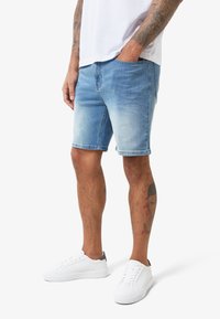 Hellblaue Denim-Shorts mit einem ausgebleichten Finish, im klassischen Schnitt, mit Seitentaschen und einem getragenen Look. Kombiniert mit weißen Sneakers.