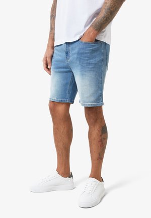 Shorts di denim azzurri chiari con un finish sbiadito, caratterizzati da un taglio classico, tasche laterali e un aspetto consumato. Abbinati a sneakers bianche.