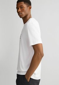 Witte t-shirt met korte mouwen, gemaakt van zachte katoen, met een ontspannen pasvorm en minimalistisch ontwerp. Gladde textuur, zonder zichtbare patronen.