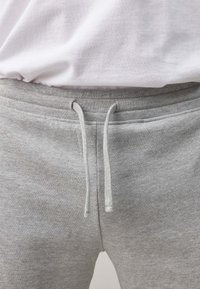 Light grey sweatpants with an elastic waistband, external drawstring, and a soft, textured fabric. Simple and functional design.