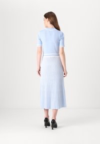 Blå plisserad midikjol med en figurnära topp, som har rundad halsringning och ribbad trim. Slät textur med kontrasterande detaljer, kombinerad med svarta klackar.