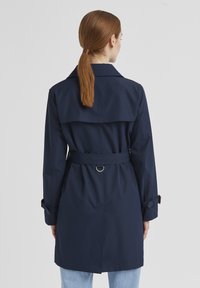 Navy wasserfester Trenchcoat mit gegürteter Taille, großem Kragen und Sturmklappe. Verfügt über verstellbare Manschetten mit Schnallendetails.