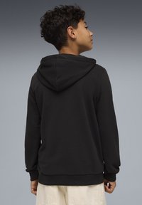 Sweat à capuche noir avec capuche visible, en tissu doux, doté de manches longues et de poignets côtelés, présenté de dos sur un fond gris.