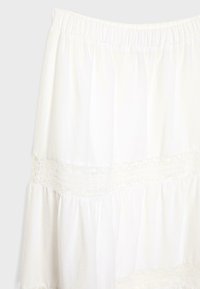 Jupe blanche à volants en tissu léger, avec une taille élastique et un ourlet en dentelle détaillé en bandes horizontales.