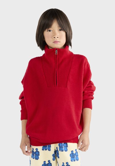 Rød strikket sweater med høj krave og halv-zip design. Har et tekstureret panel på brystet og en løs pasform. Bæres sammen med mønstrede bukser.