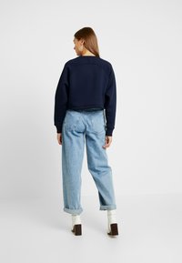 Námornícky cropped sveter s rebrovanými manžetami a lemom, kombinovaný s svetlomodrými voľnými džínsami. Model má na sebe biele členkové čižmy na podpätku.