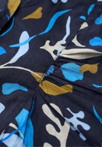 Mörk tyg med rynkad söm som har ett abstrakt botaniskt mönster i blå, beige och senapsgula former.