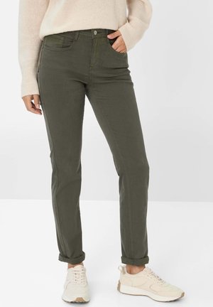 Olivgrüne Hosen mit geradem Schnitt, hoher Taille, Eingrifftaschen und umgeschlagenen Säumen, kombiniert mit hellbeigen Sneakern.