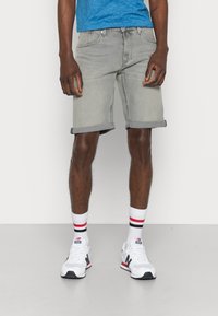 Pantalones cortos de mezclilla gris con puños enrollados, combinados con calcetas blancas con rayas rojas y negras, y zapatillas blancas. Camiseta azul visible.