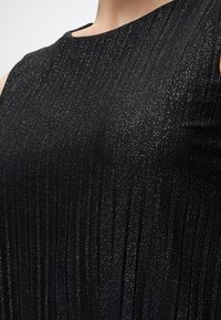 Gros plan d'une robe noire sans manches avec des plis verticaux et petits points de paillettes argentées sur tout le tissu.