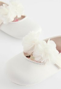 Weiße Ballettschuhe aus Stoff mit weichen Blumenverzierungen auf der Vorderseite, abgerundeter Zehenpartie und gemusterten Innensohlen. Glatte Oberfläche, dezenter Glanz.