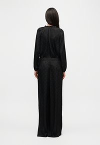 Μαύρη ολόσωμη φόρμα με μακριά μανίκια, υφή με μοτίβο διαμαντιού, ελαστική μέση και βολάν στο λαιμό, με φαρδιά ανοίγματα στα πόδια και χαλαρή εφαρμογή.