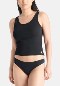 Schwarzes geripptes Tanktop mit einem runden Ausschnitt, versehen mit einem kleinen weißen Logo an der unteren linken Seite, kombiniert mit passenden schwarzen Bikinihosen.